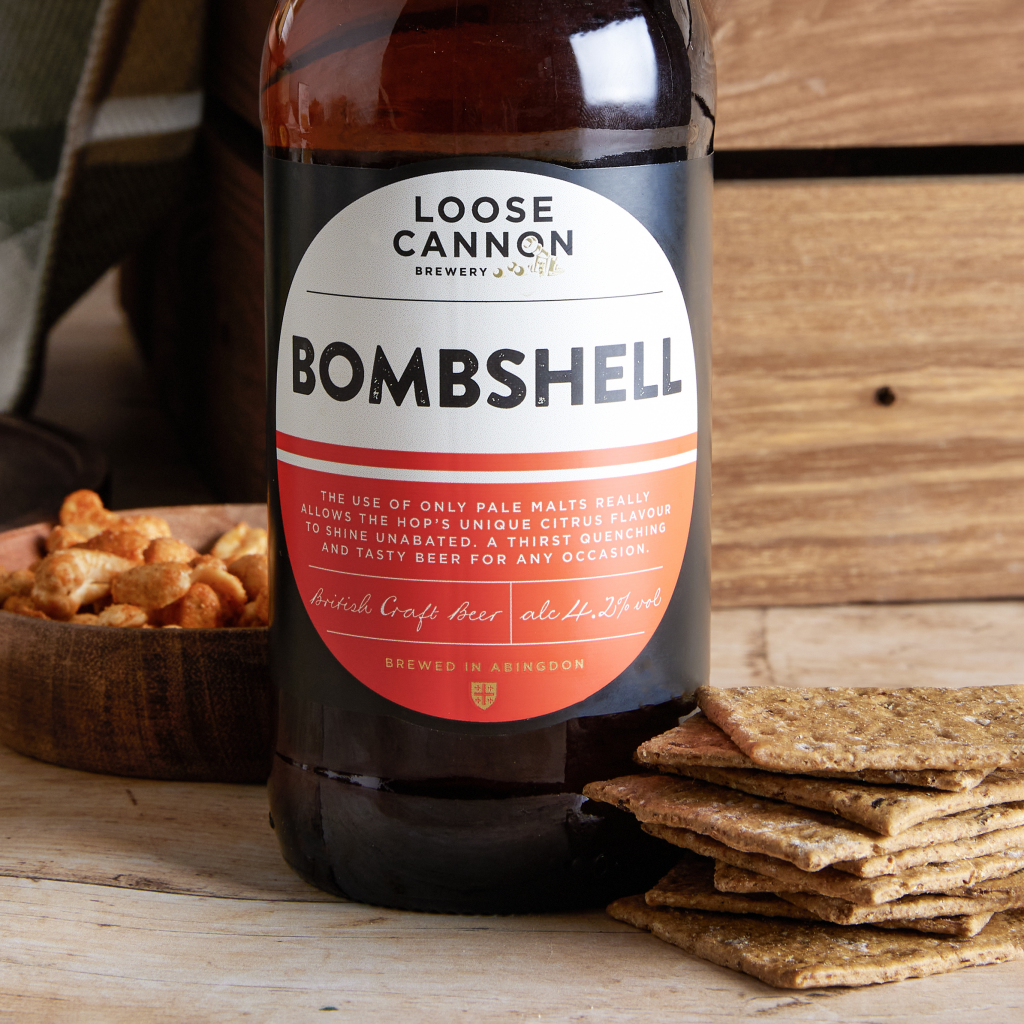 This image shows a man drinking Loose Cannon Brewery's Bombshell Pale Ale. This beer has a red label and is included in a gift hamper curated by hampers.com called The Gentleman's Tea Hamper.